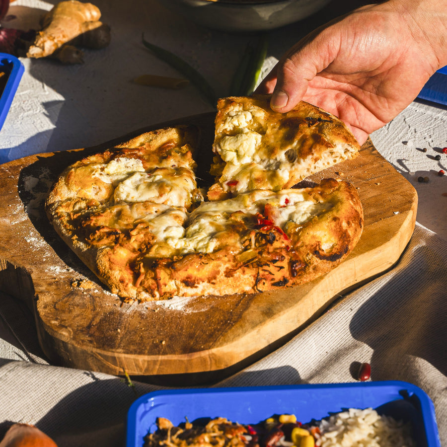 A hand takes a slice of SportMeals High Protein Pinsa with pulled chicken off the board