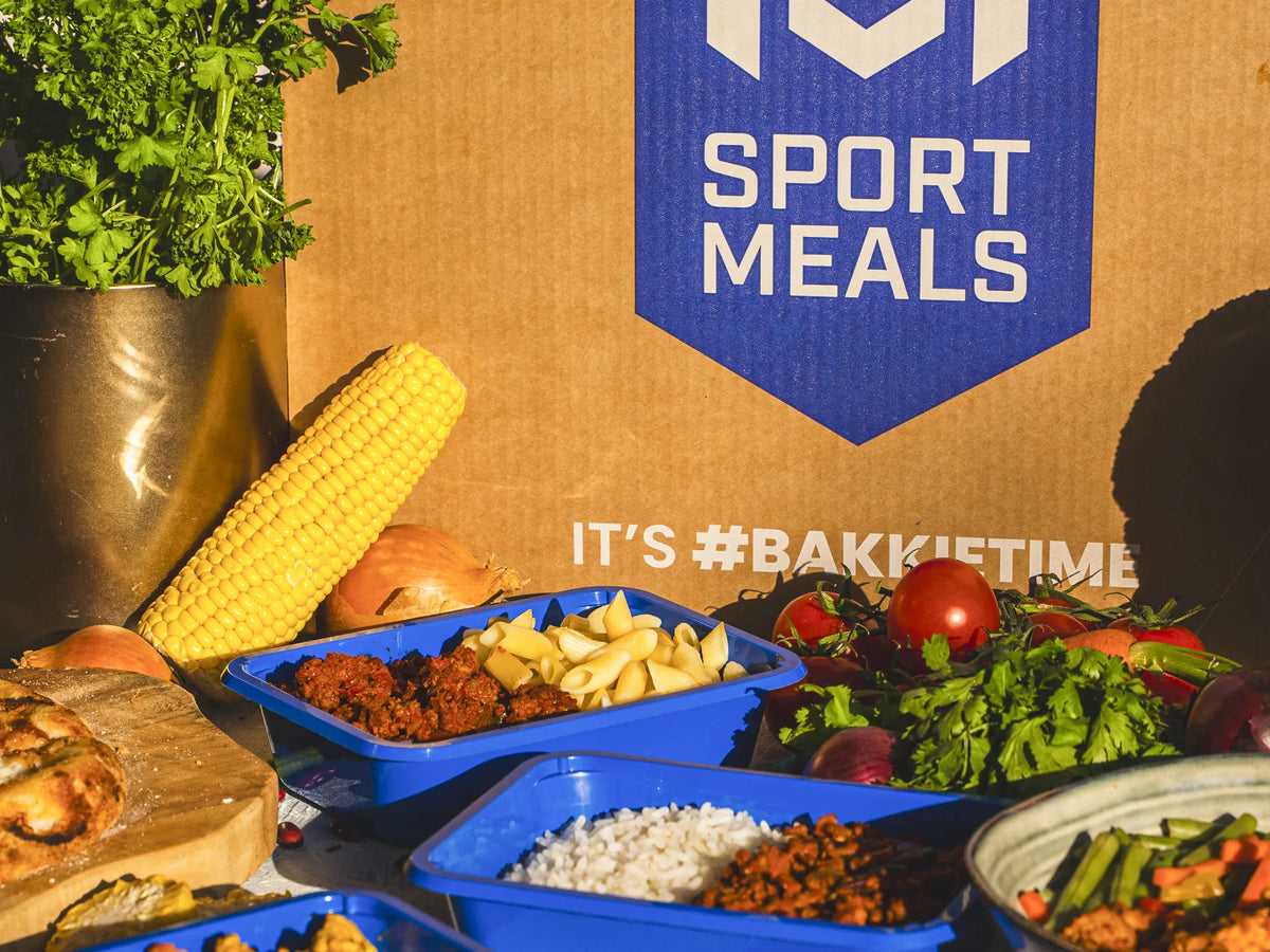 Een SportMeals-doos met daarvoor een tafel vol maaltijden