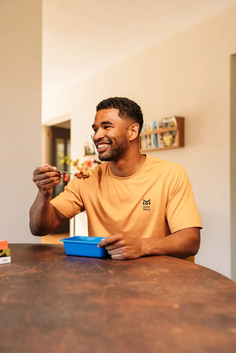 Bob eet aan tafel in een lichte woonkamer uit een blauwe SportMeals-maaltijd