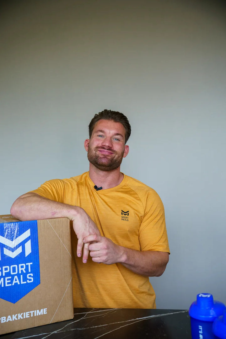 Joey leunt lachend op een SportMeals-doos