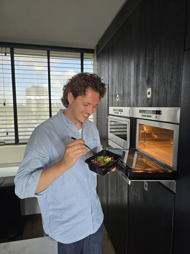 Delano haalt een opgewarmde maaltijd uit de oven en eet uit het bakje