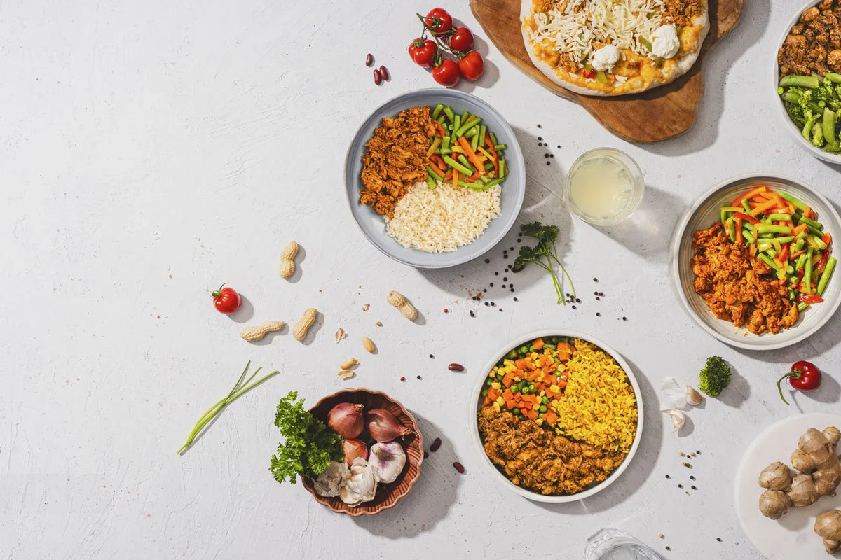 Bovenaanzicht van opgediende SportMeals-maaltijden op borden: bolognese, rijstmaaltijden met kip en groente, en een pinsa