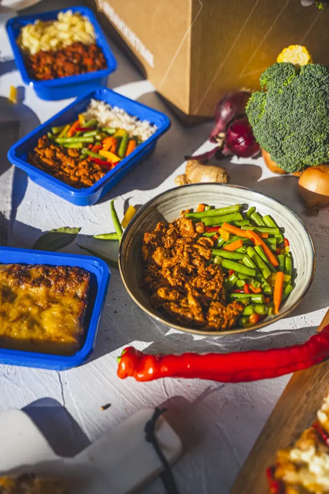Blauwe SportMeals-maaltijden met rijst, groente, kip en bolognese naast een verzenddoos