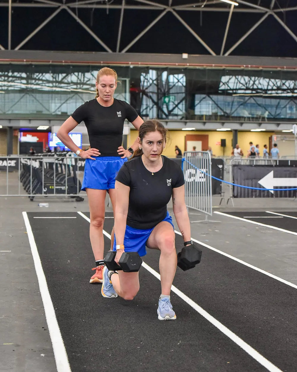 Twee deelnemers doen lunges met dumbbells tijdens de Gym Race