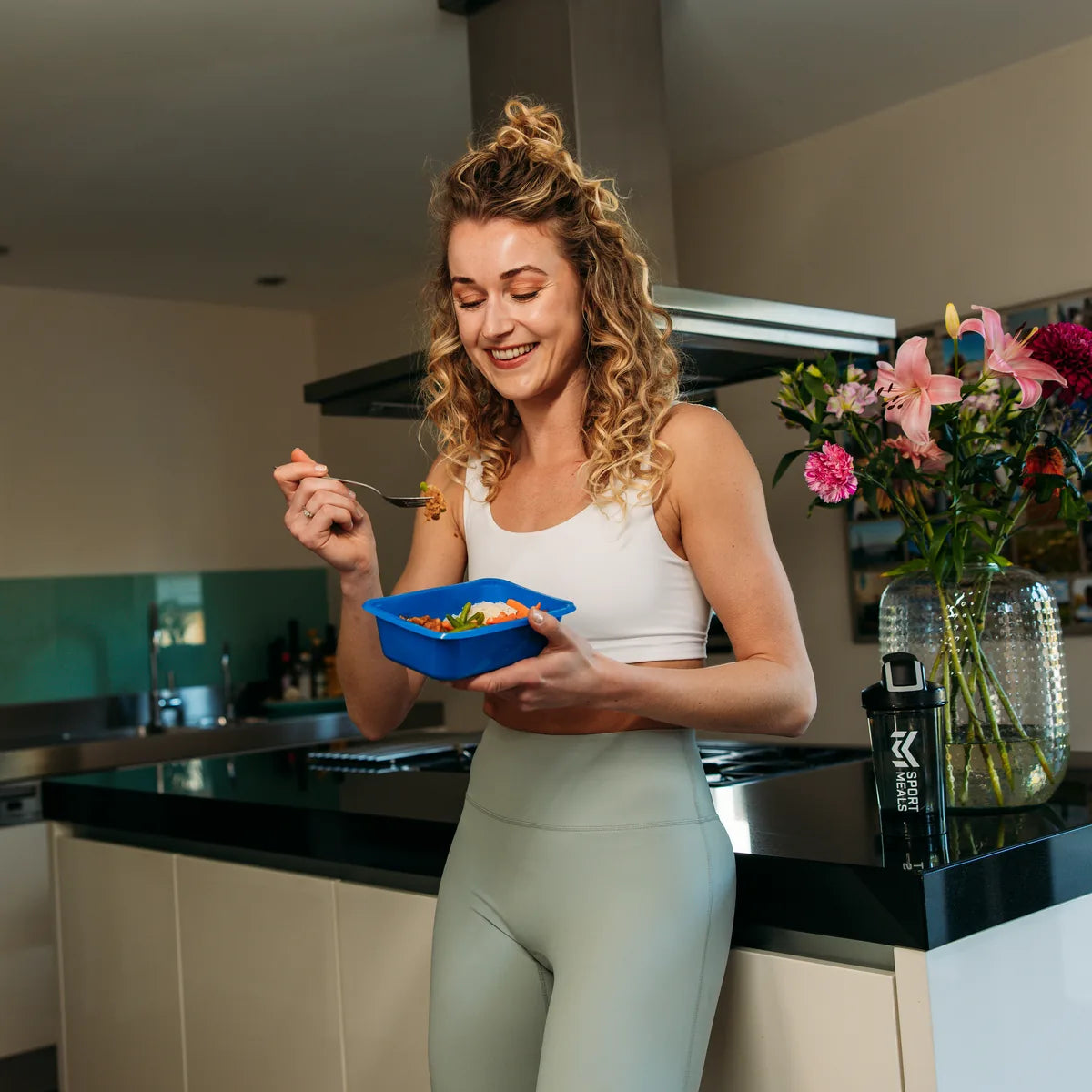 Woman eating at home in the kitchen from a blue SportMeals tray