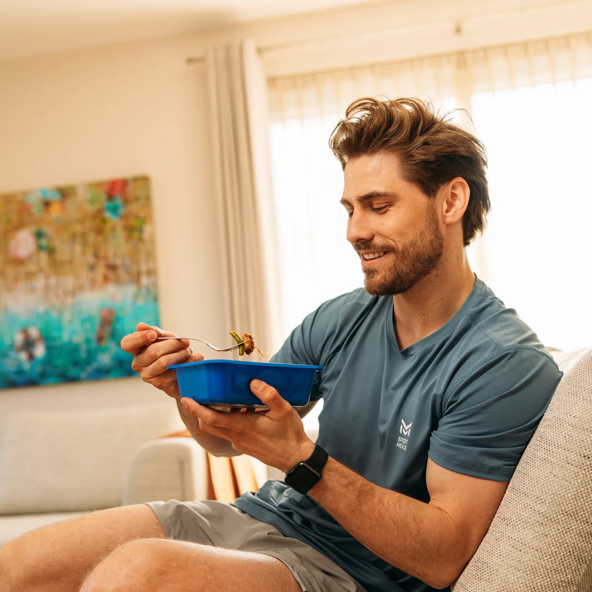Man eet op de bank uit een blauw SportMeals-bakje