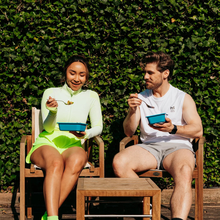 Twee sporters eten buiten uit blauwe SportMeals-bakjes