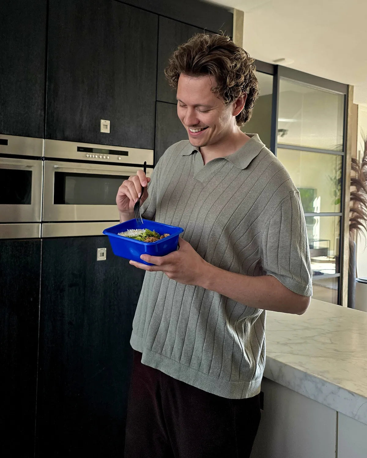 Man eet in de keuken uit een blauw SportMeals-bakje