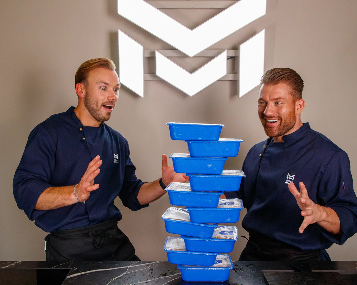 Oprichter Joey en Ronald van SportMeals lachend naast een toren van blauwe bakjes