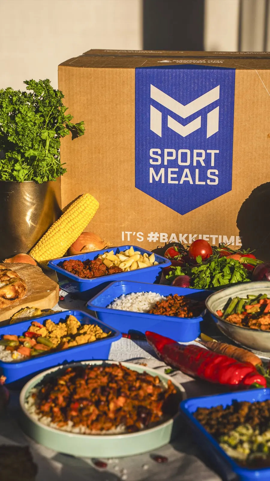 Een SportMeals-doos met daaromheen maaltijden in blauwe bakjes en op borden